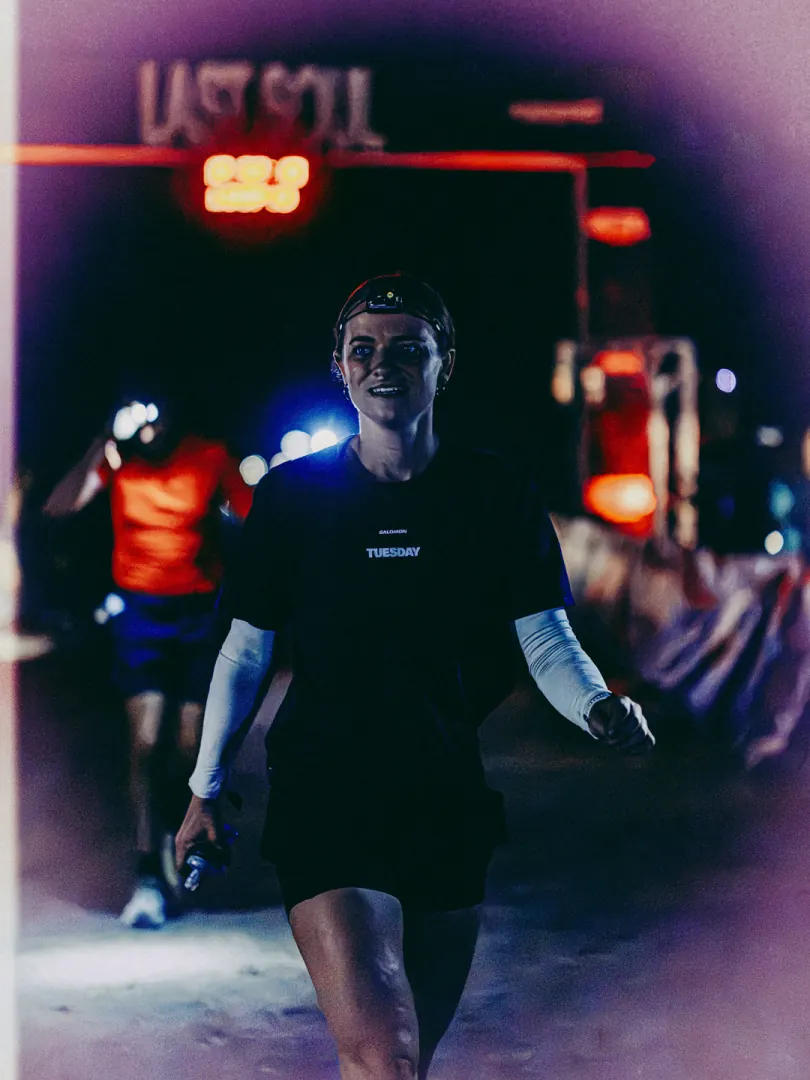 A runner in a dark shirt walks out of the red-lit start gantry at night.