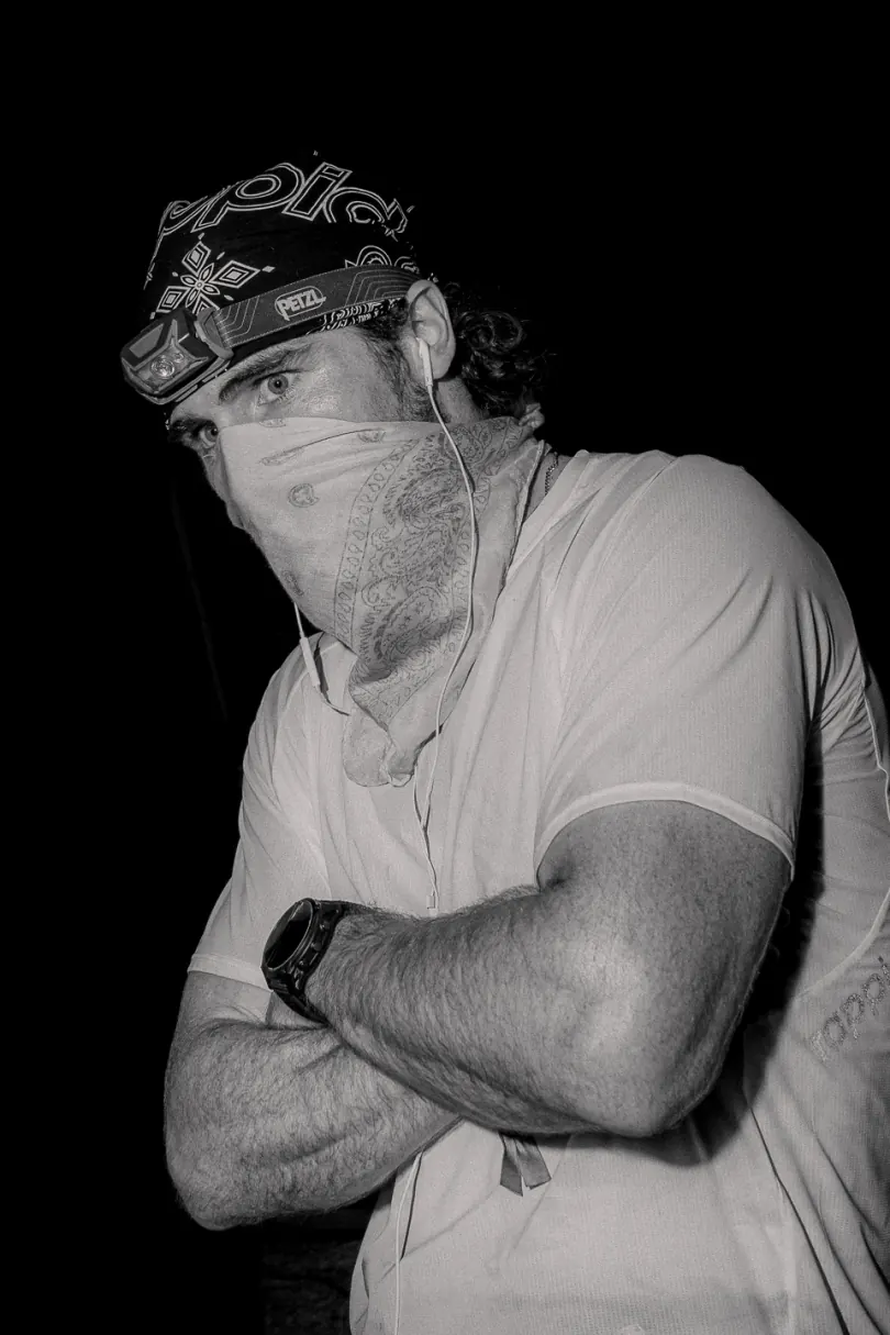 A black-and-white portrait of a runner in a bandana and face covering, arms crossed.