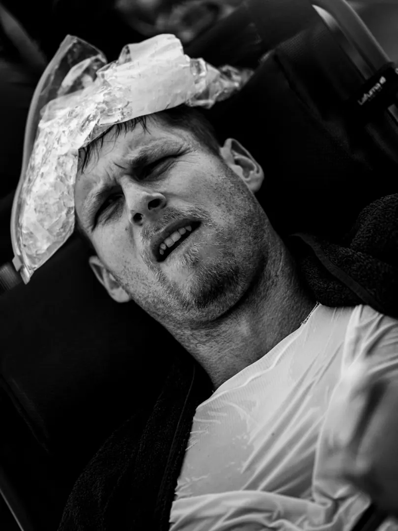 A runner with an ice pack on his head, eyes shut, exhausted.