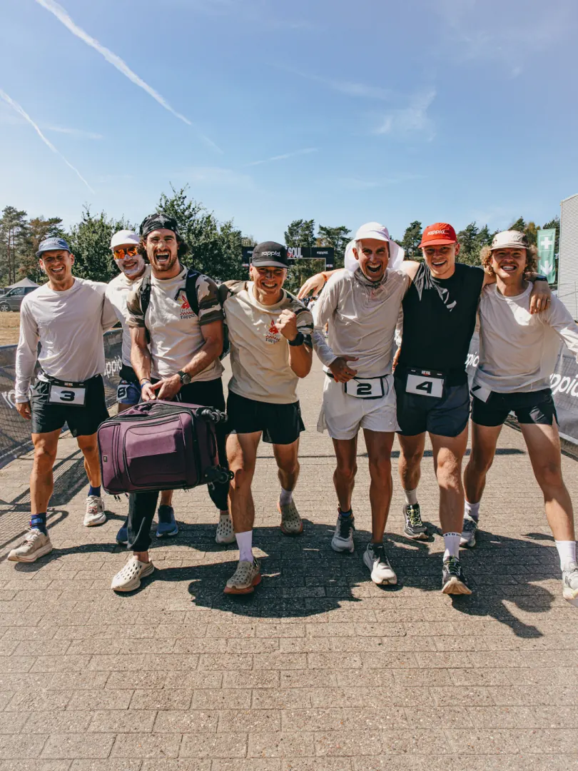 A group of runners with their arms round each other in the sun, bags at their feet.