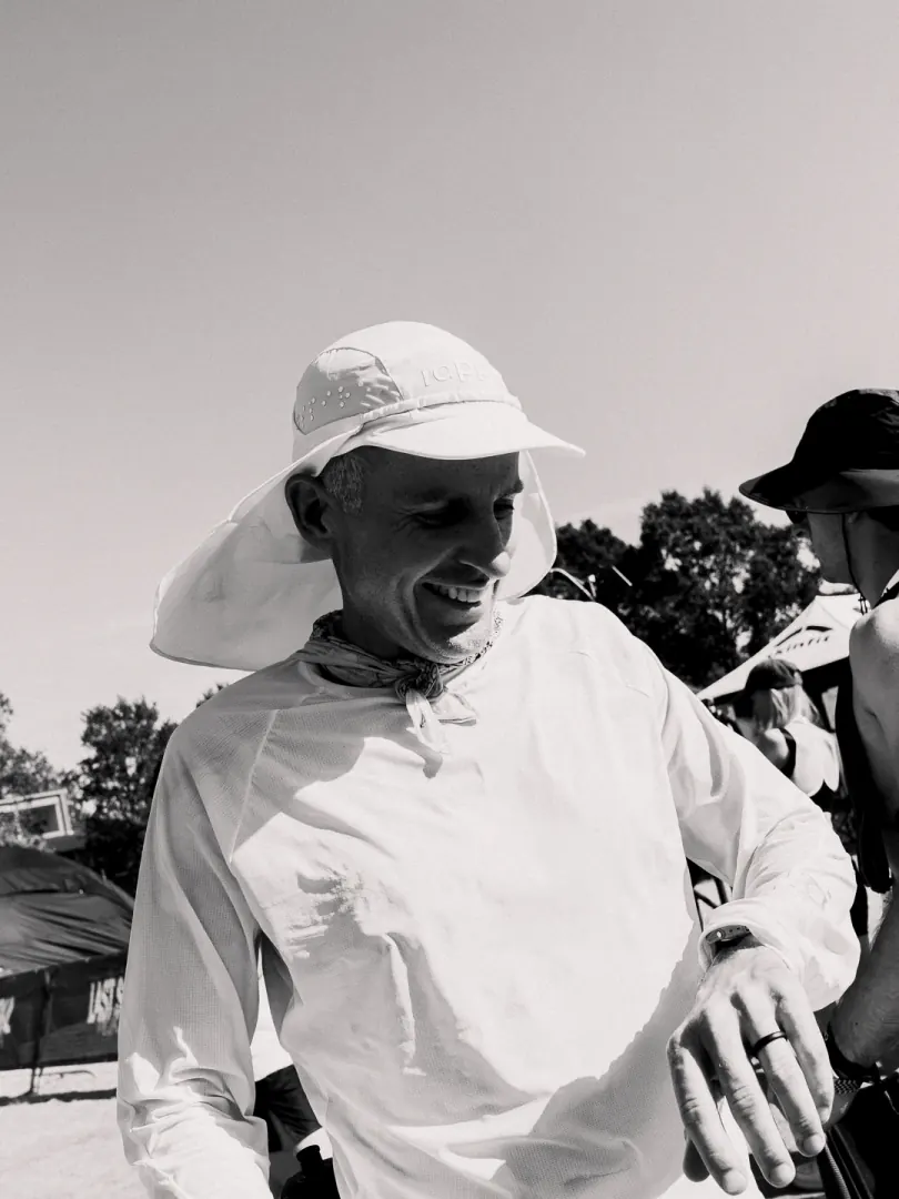 A runner in a white sun hat and neck cover looks down at his watch.