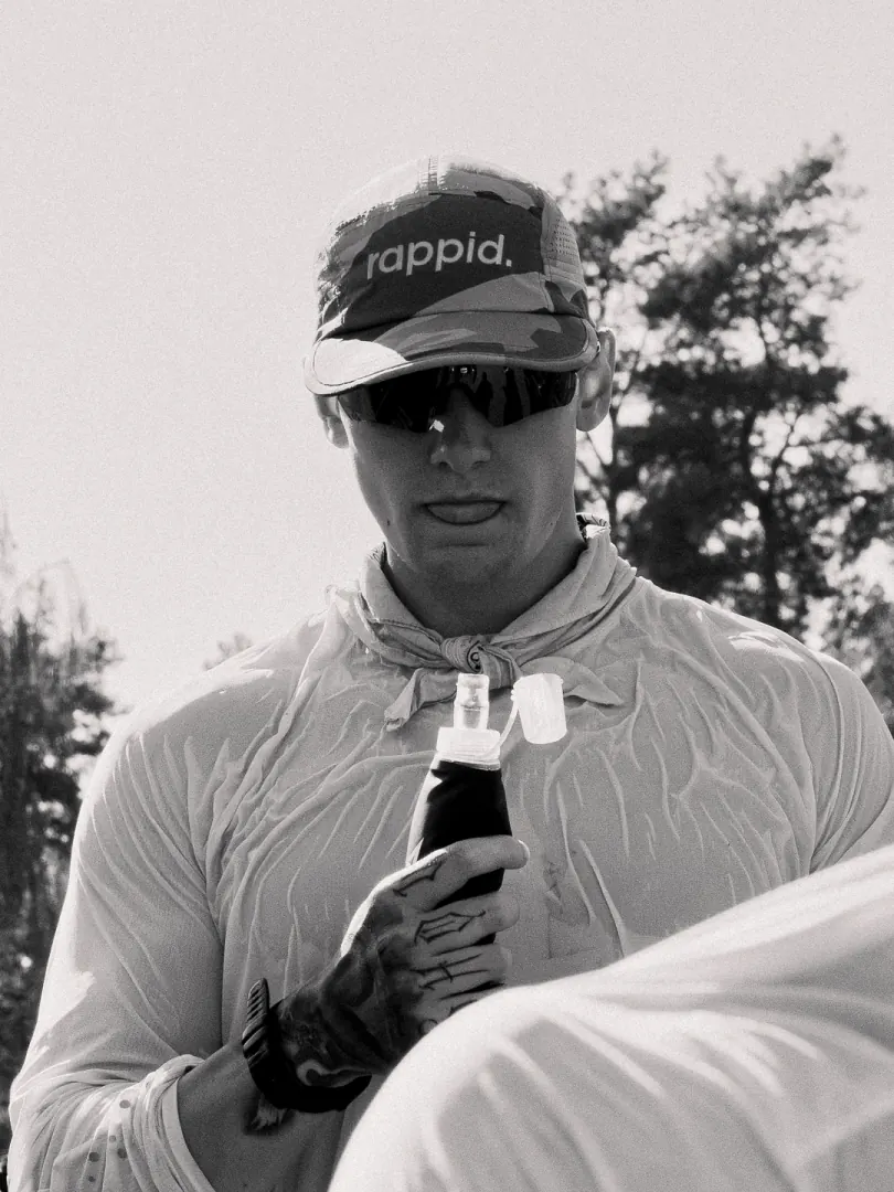 A runner in a cap and sunglasses holds a bottle, in black and white.