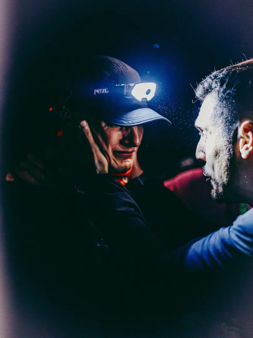 Two men in head torches talk close together in blue light.