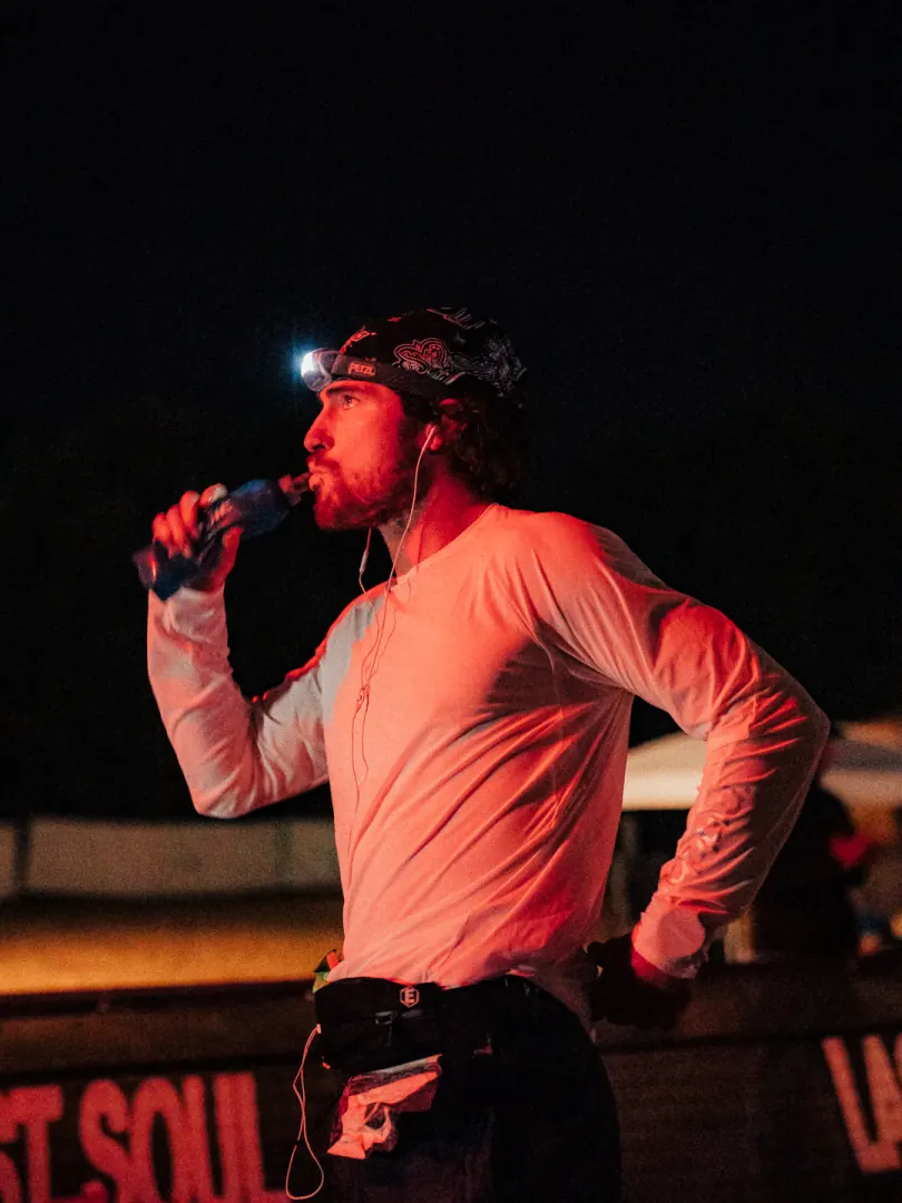 A runner in a head torch drinks on the loop, lit red.