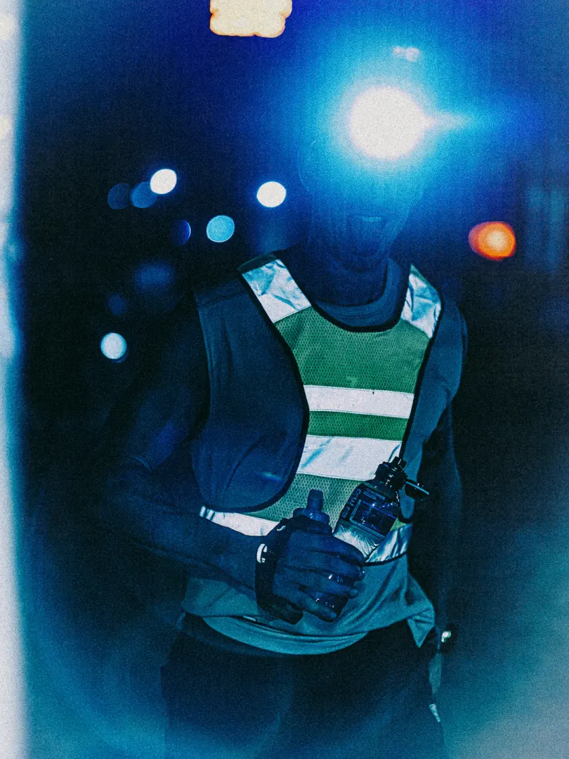 A runner in a green hi-vis vest and head torch, lit blue.