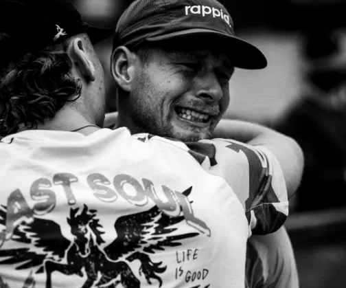 A runner in a rappid. cap in tears, hugging a supporter in a Last Soul T-shirt