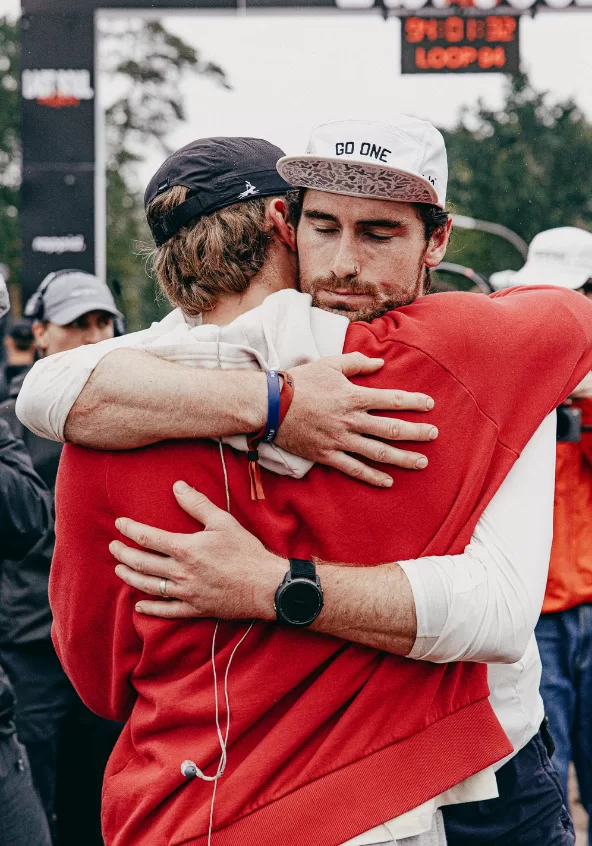Two runners embracing beneath the race clock at loop 94