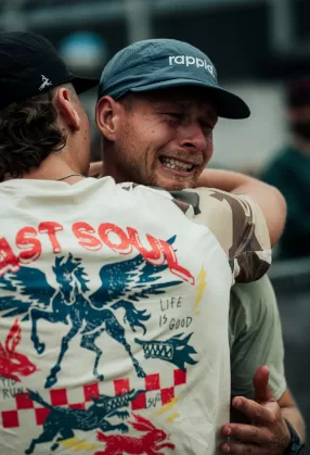 A runner in a rappid. cap weeping on a supporter’s shoulder