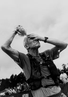 An older runner pours water over their head, one hand over their eyes